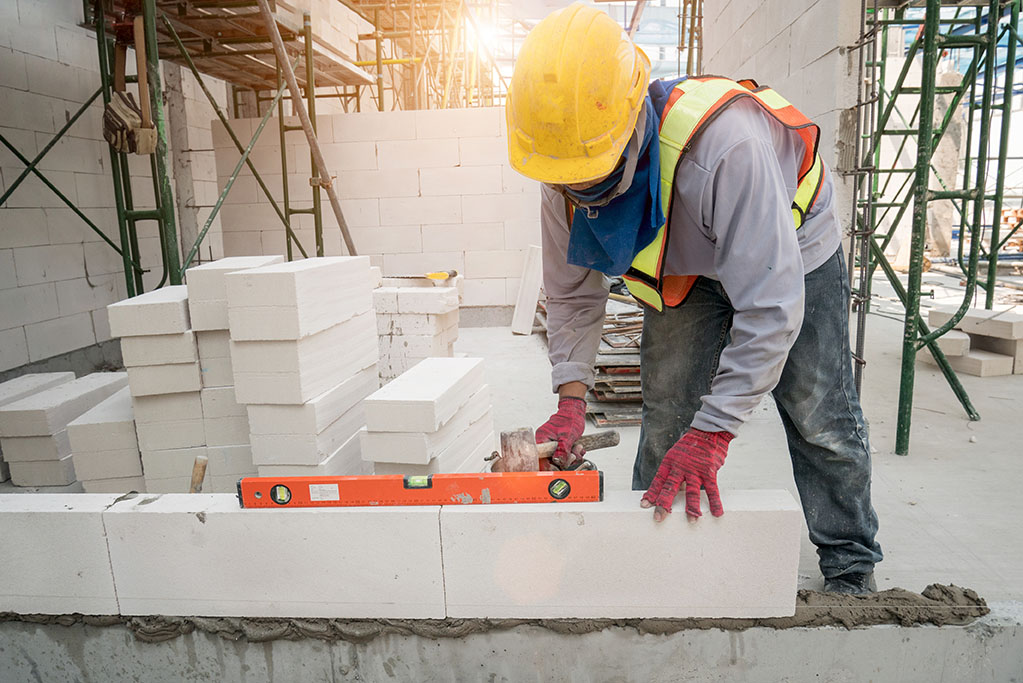 Masonry construction worker in standard safety uniform install concrete block wall on new home construction site