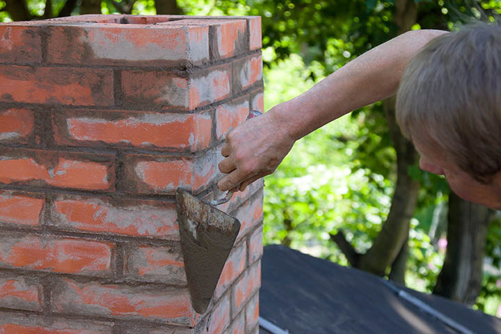 A masonry worker, working with a trowel and making a chimney of red bricks